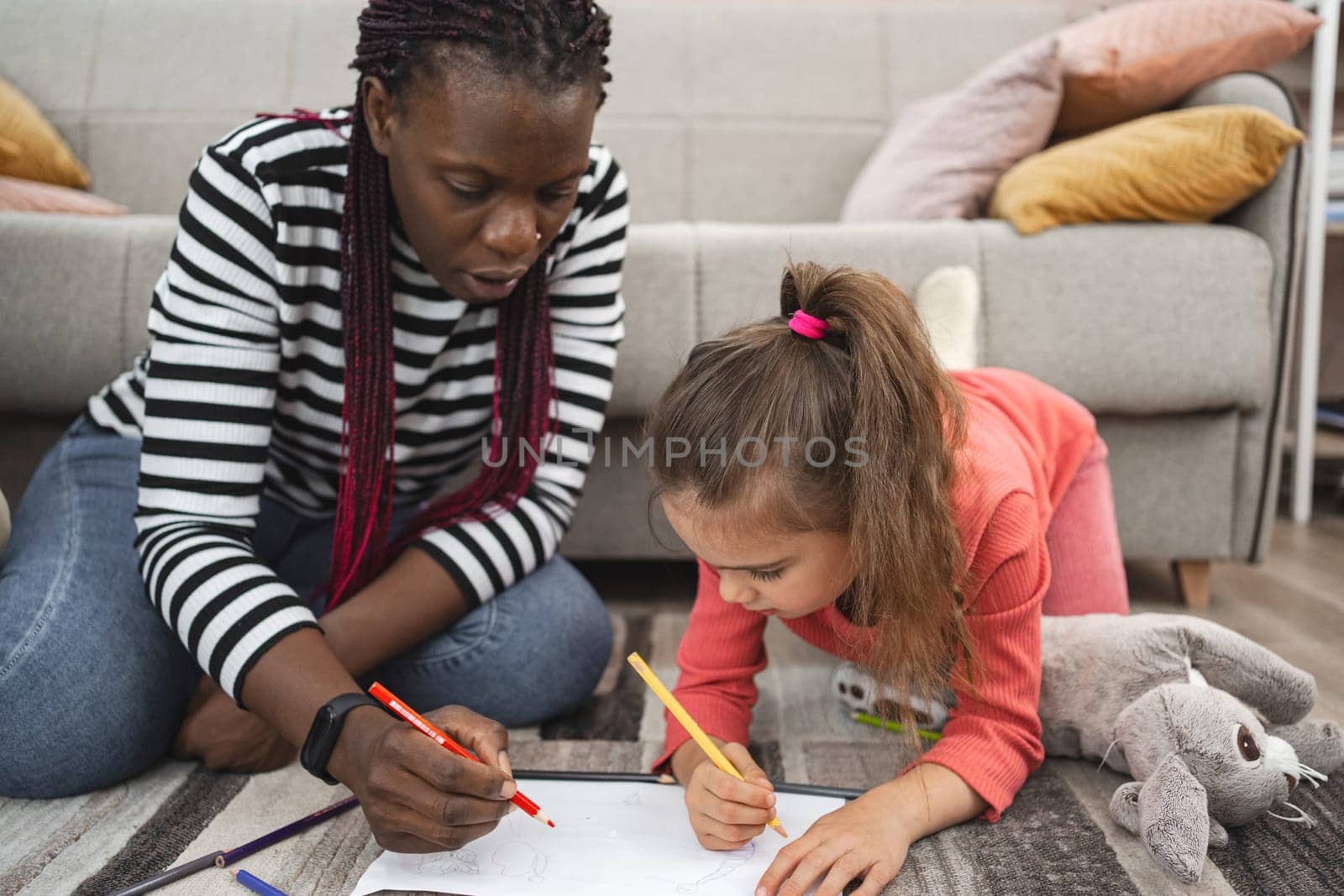 A mother and daughter draw together on the living room floor with crayons.