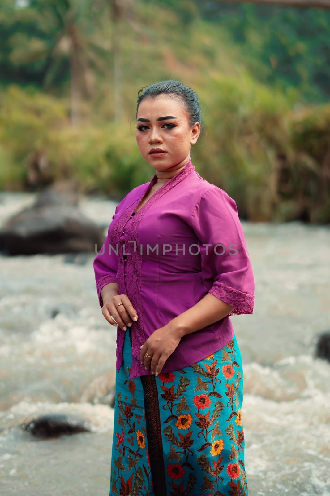 Asian woman standing in front of the river while wearing a purple dress with beautiful makeup and river in the background inside the village