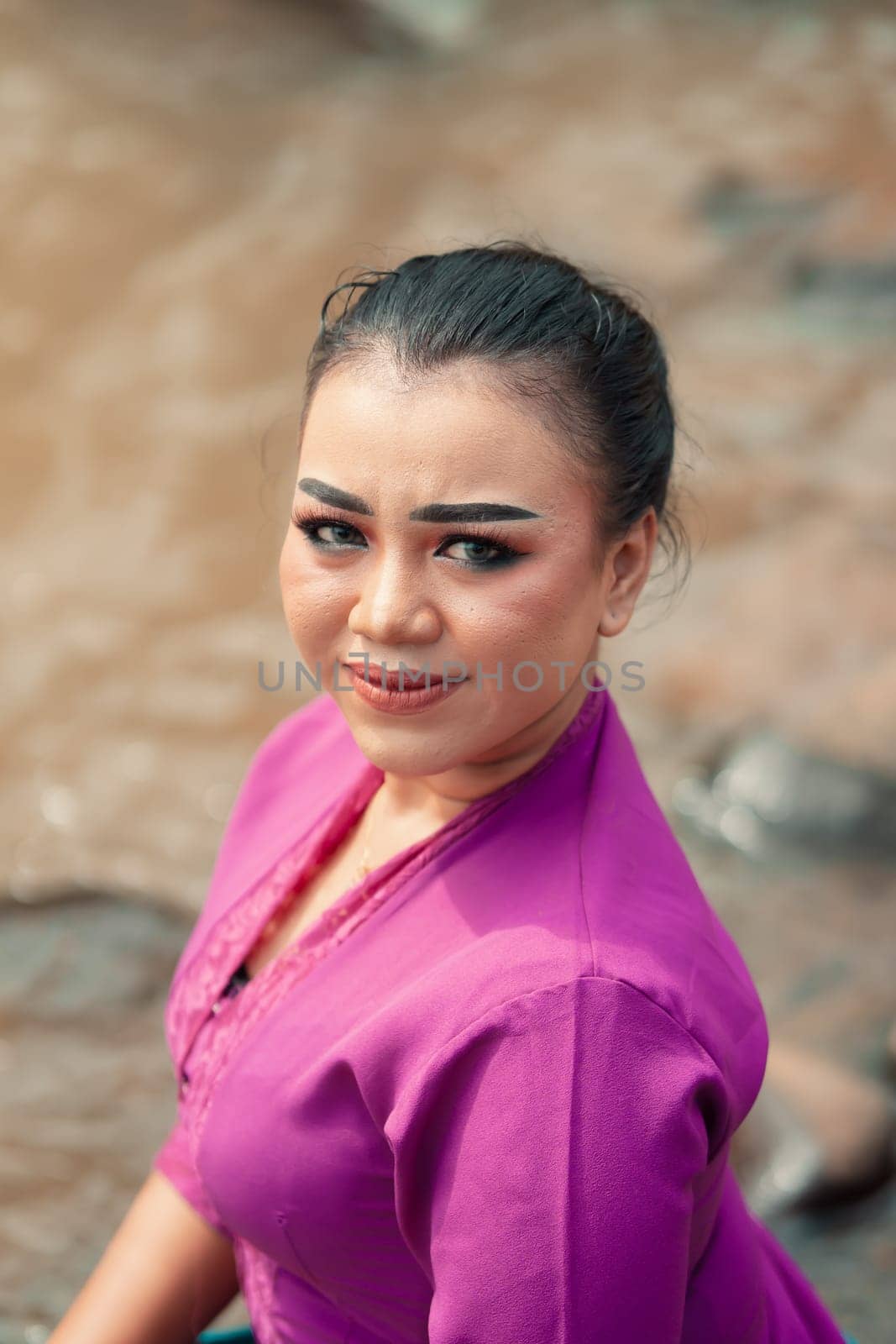 A close-up shot of a beautiful Asian woman with makeup while wearing a traditional purple dress called kebaya near the river