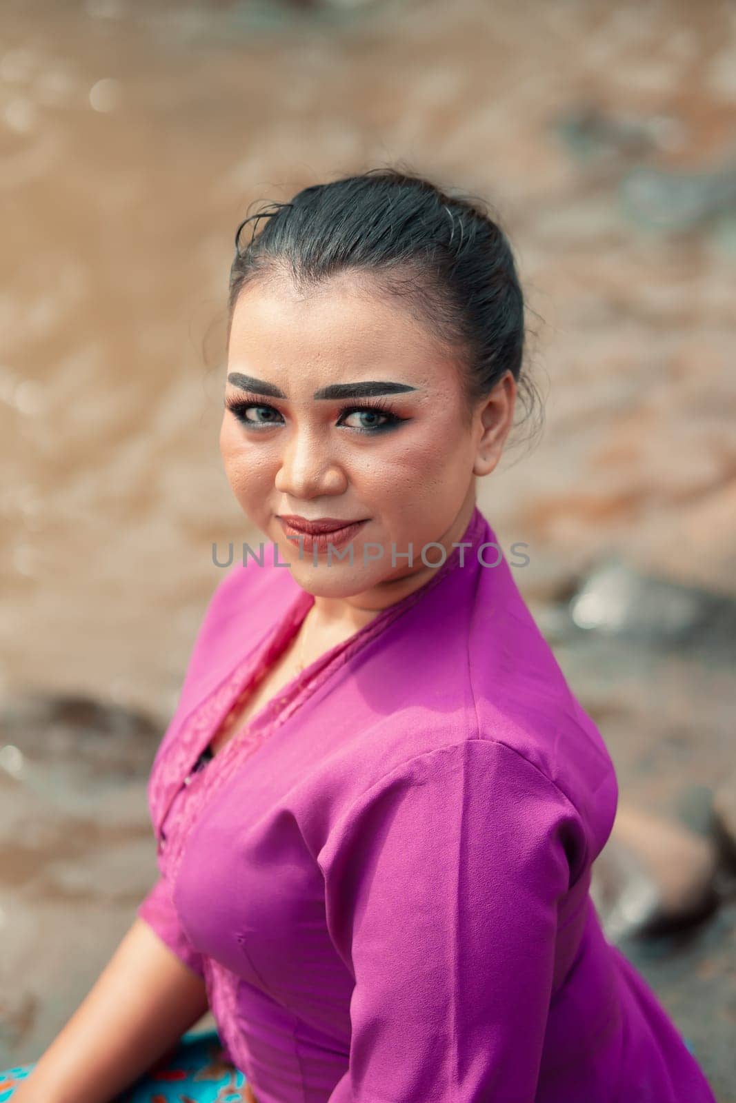 A close-up shot of a beautiful Asian woman with makeup while wearing a traditional purple dress called kebaya near the river