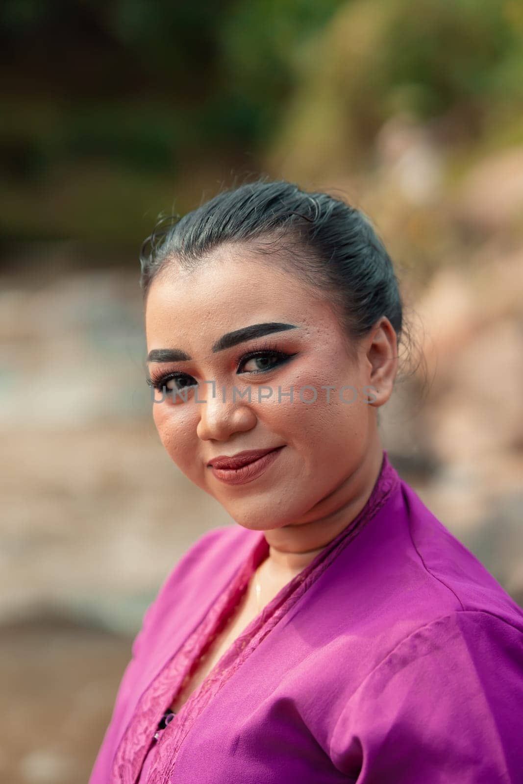 A close-up shot of a beautiful Asian woman with makeup while wearing a traditional purple dress called kebaya near the river