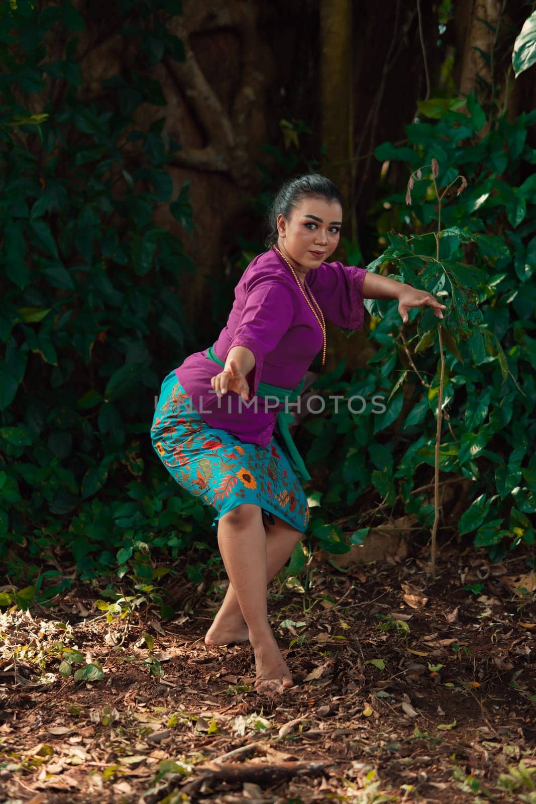 Sexy Sundanese woman with purple dress dancing in front of the big tree and the green leaves in the background during the daylight
