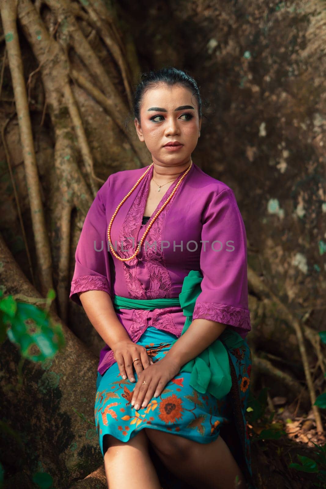 An Asian woman beautifully sitting on the big tree in a purple dress while visiting the jungle in the daylight