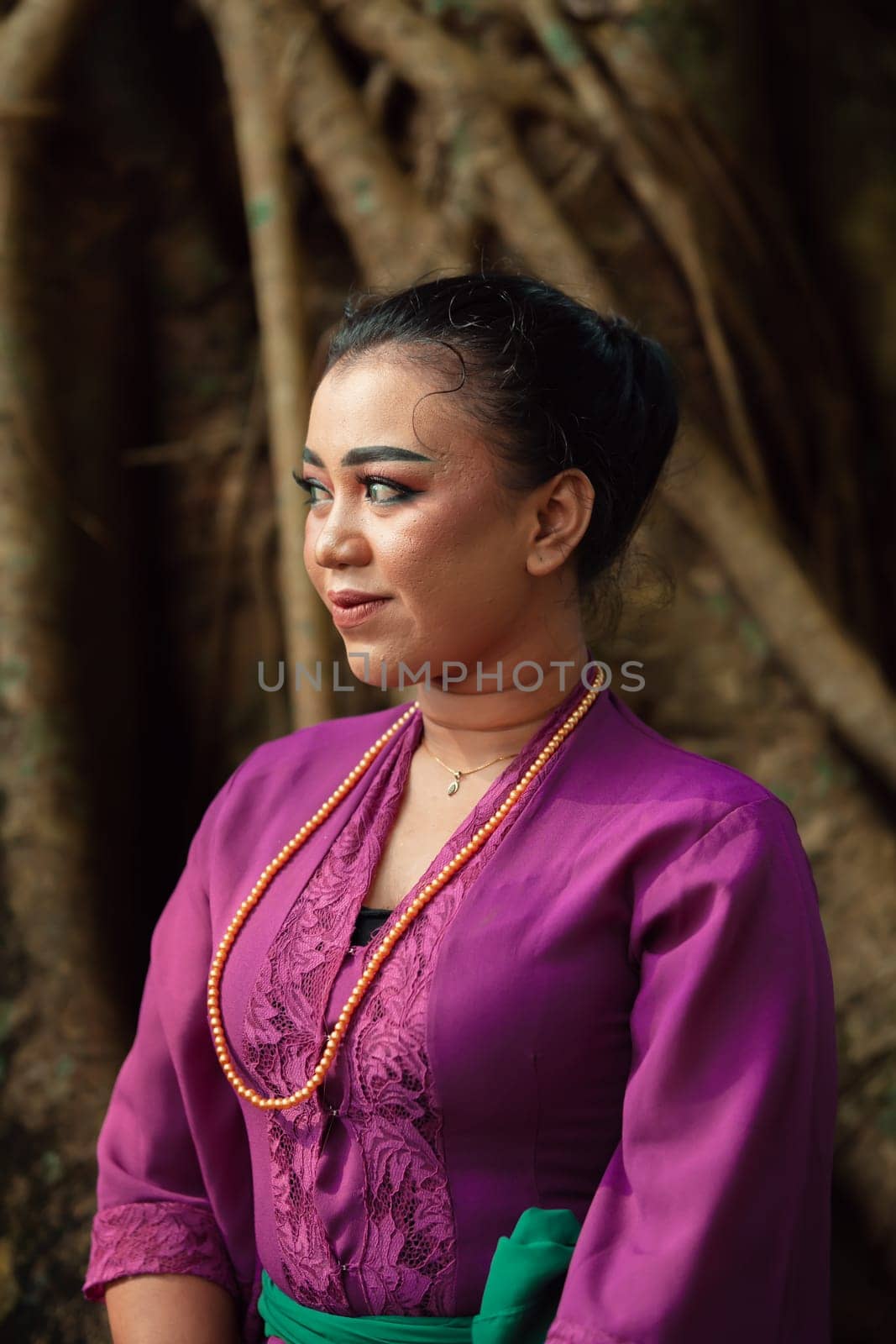 An Asian woman beautifully sitting on the big tree in a purple dress while visiting the jungle in the daylight