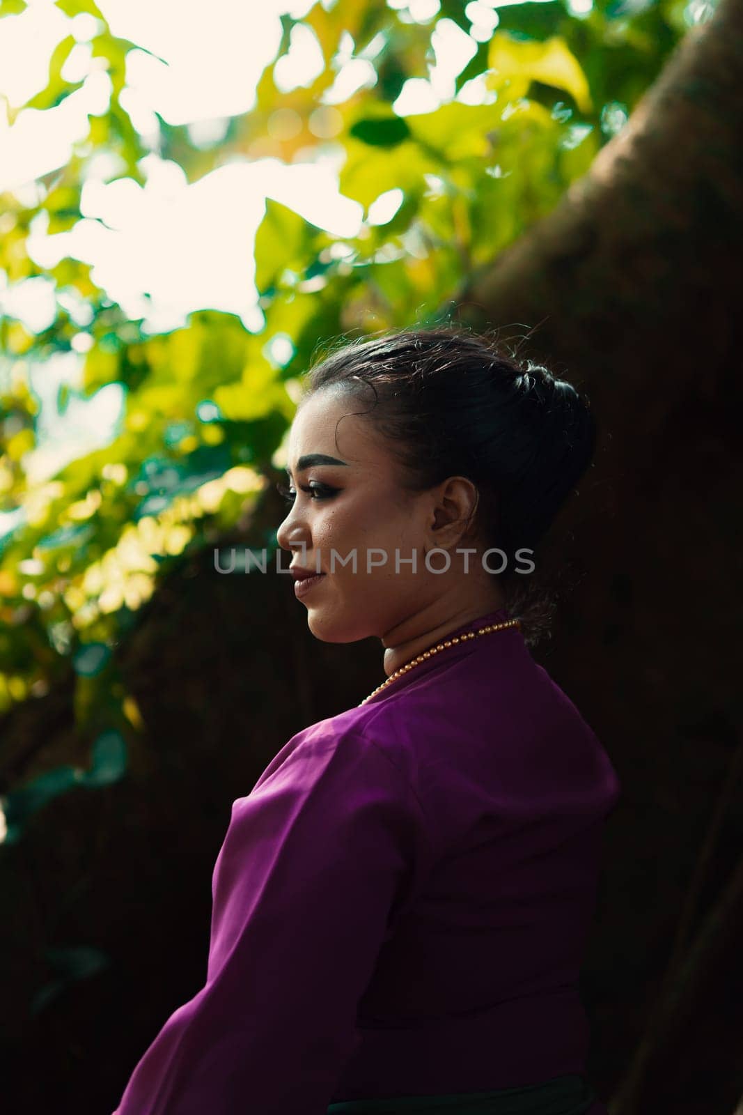 An Asian woman beautifully sitting on the big tree in a purple dress while visiting the jungle in the daylight