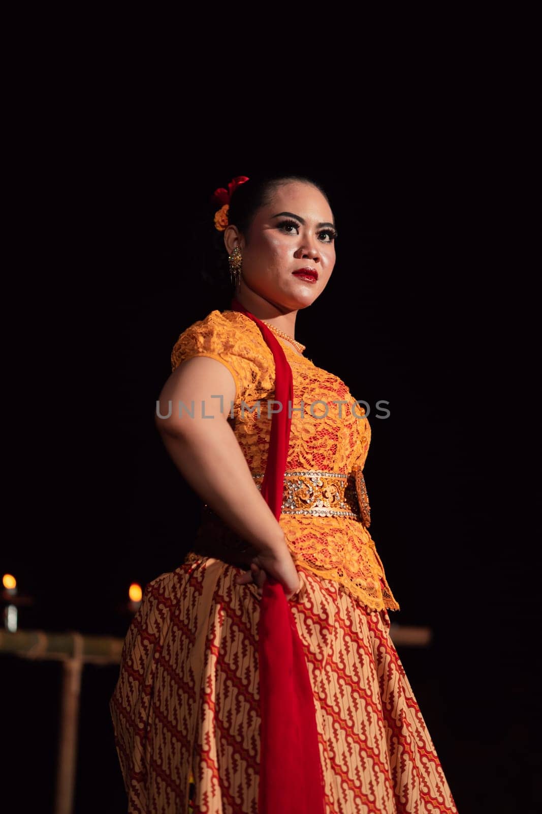 Brave Balinese woman poses with an angry expression while wearing a traditional orange dress and makeup during the dance festival