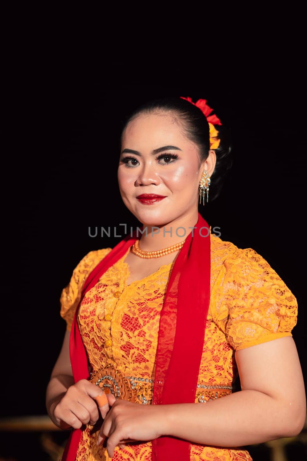 Cute Indonesian woman with red lips and a red scarf wearing a traditional Sundanese dress called kebaya inside the dance festival