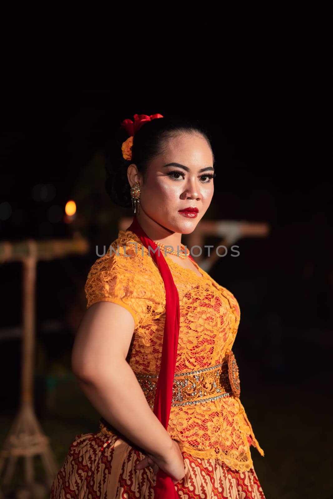 Brave Balinese woman poses with an angry expression while wearing a traditional orange dress and makeup during the dance festival