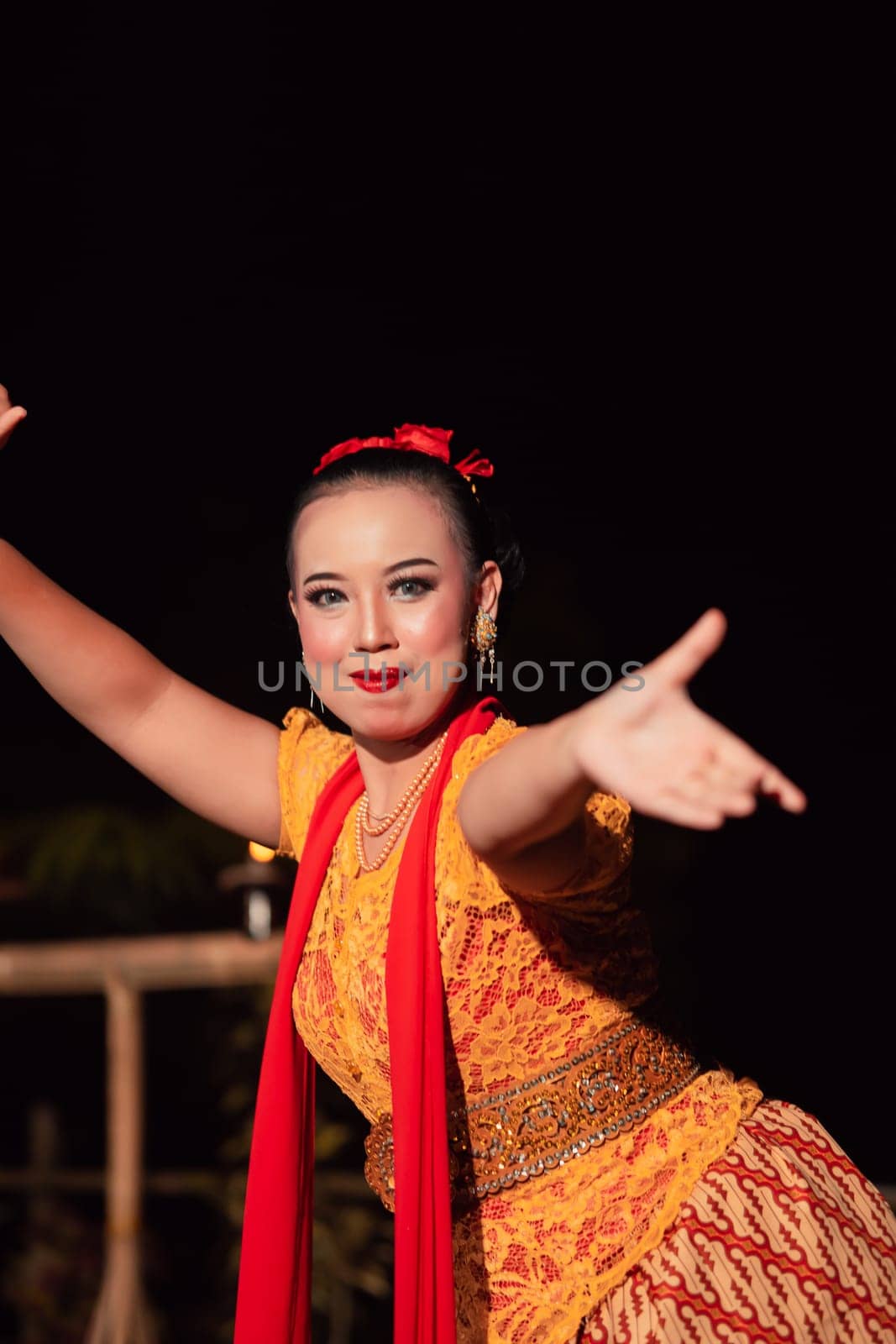 Balinese dancer with an orange costume and wearing makeup posing like a dancer while in black hair inside the village