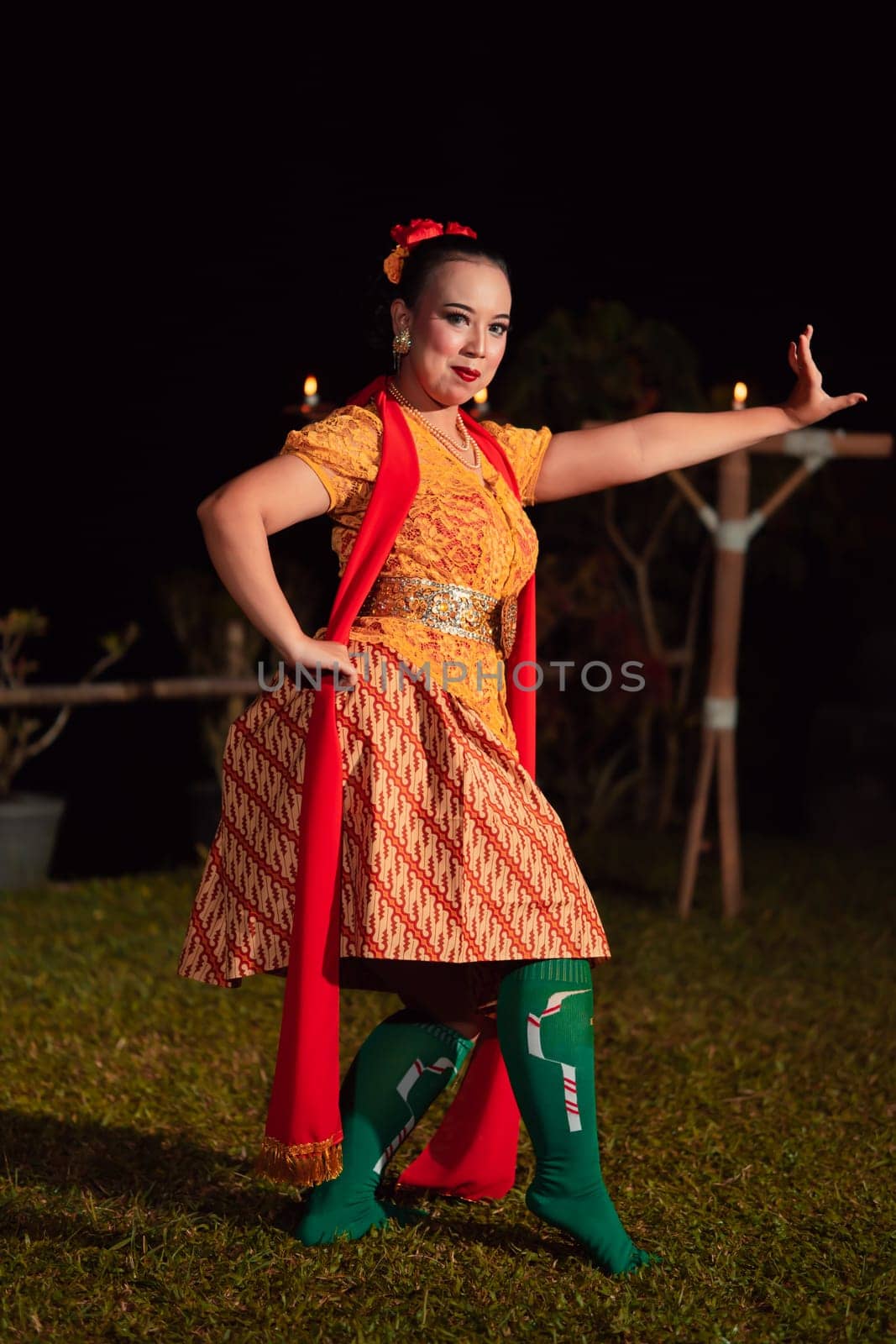 Balinese dancer with an orange costume and wearing makeup posing like a dancer while in black hair inside the village