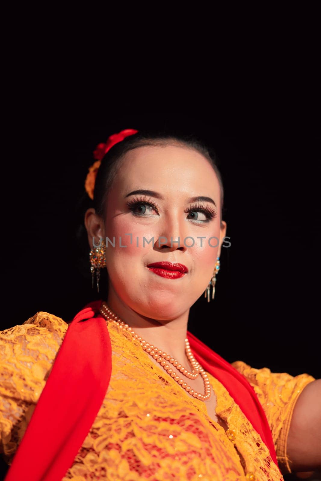 Indonesian woman in makeup with red lips wearing a golden necklace and golden earrings before dancing on the stage