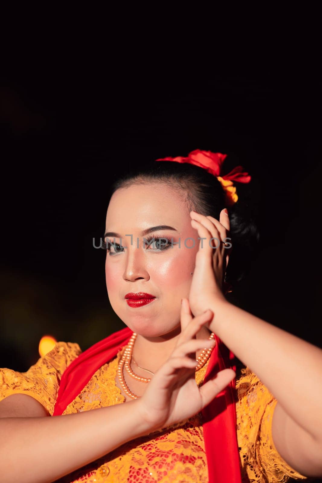Indonesian woman in makeup with red lips wearing a golden necklace and golden earrings before dancing on the stage