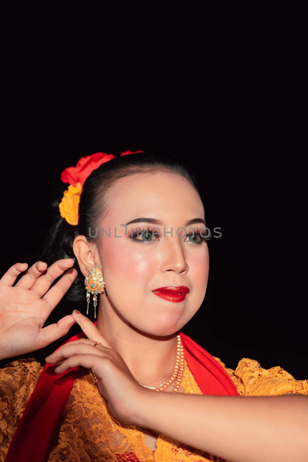 Exotic Javanese woman wearing beautiful makeup with red lips while wearing a traditional yellow costume and red scarf inside the village