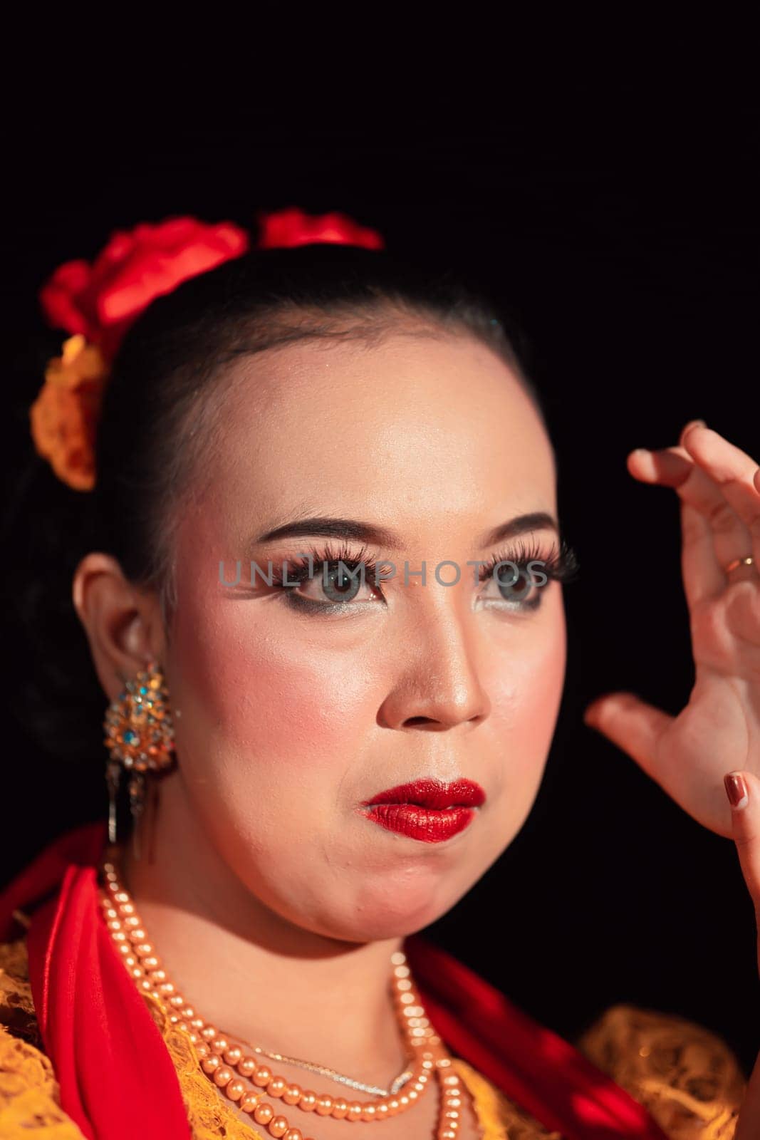 Exotic Javanese woman wearing beautiful makeup with red lips while wearing a traditional yellow costume and red scarf inside the village
