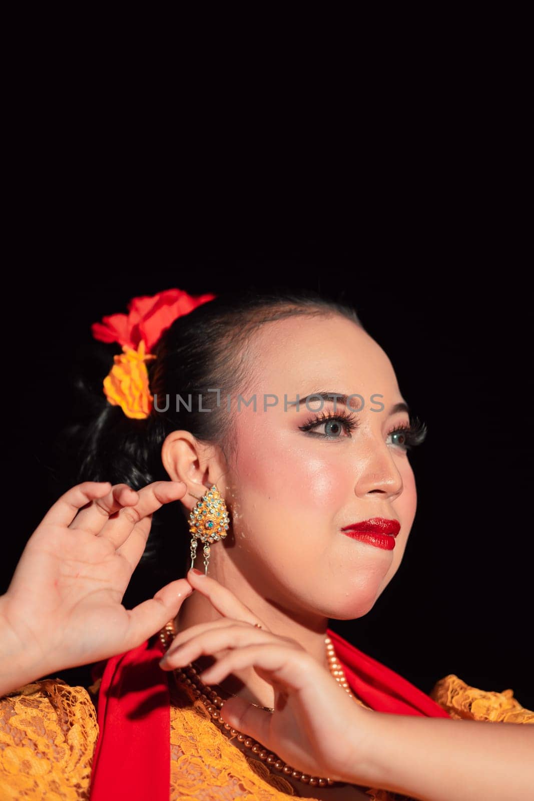 Exotic Javanese woman wearing beautiful makeup with red lips while wearing a traditional yellow costume and red scarf inside the village
