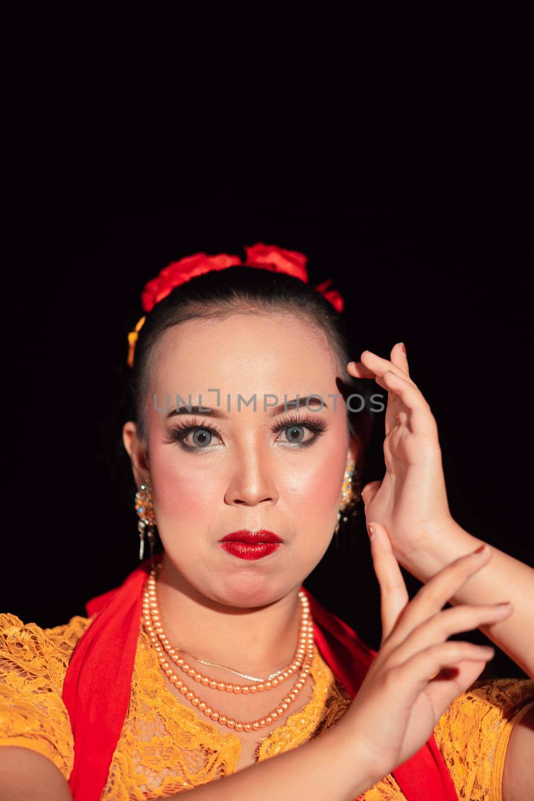 Indonesian woman in makeup with red lips wearing a golden necklace and golden earrings before dancing on the stage