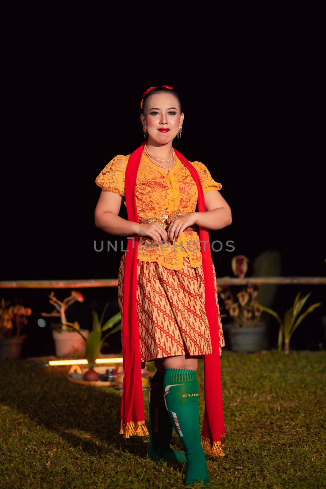 Indonesian woman with a gorgeous orange batik dress wearing a red scarf and red lips on her face standing inside the stage