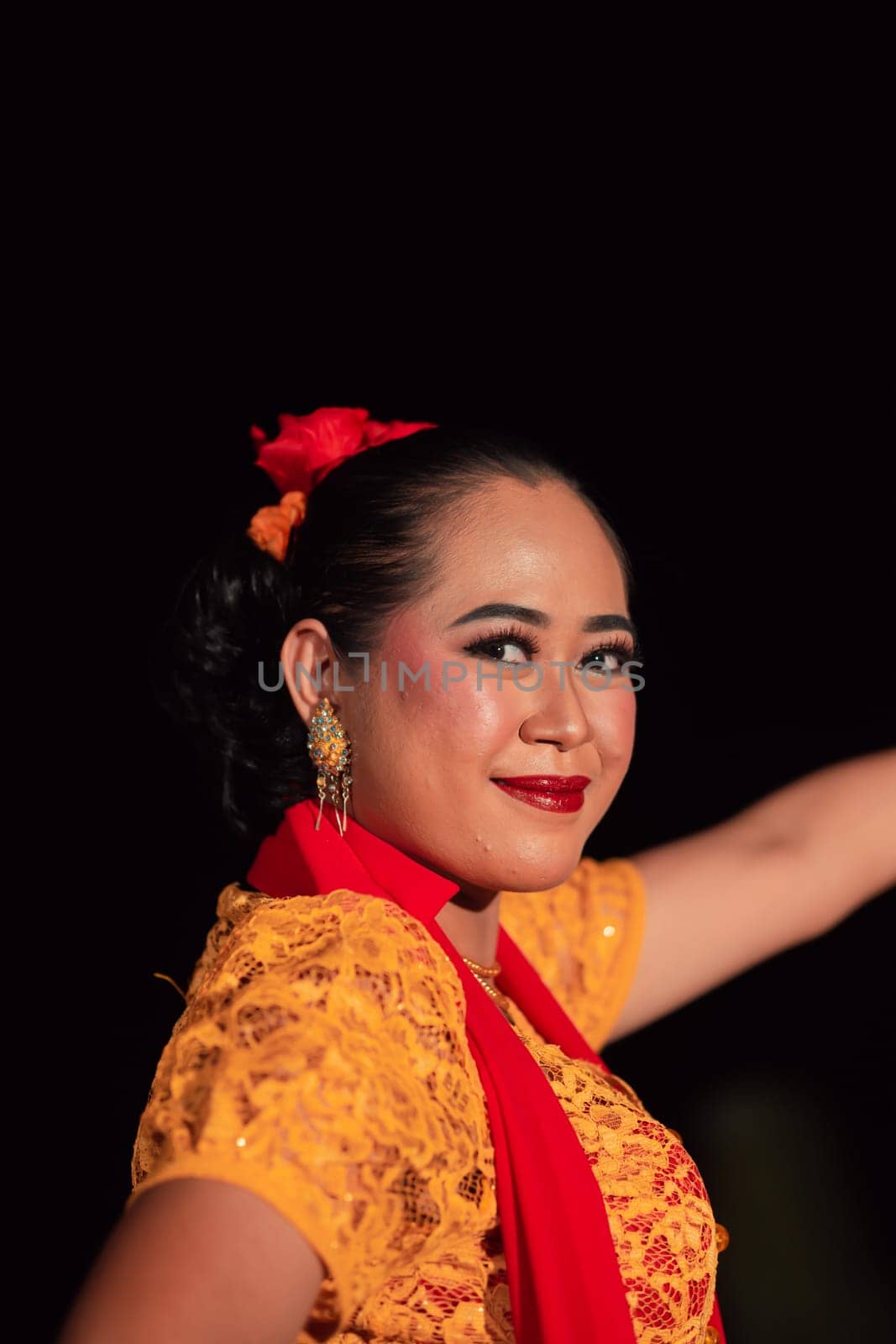 Close-up face of a Balinese woman during the traditional dance performance while wearing an orange costume and makeup on the stage