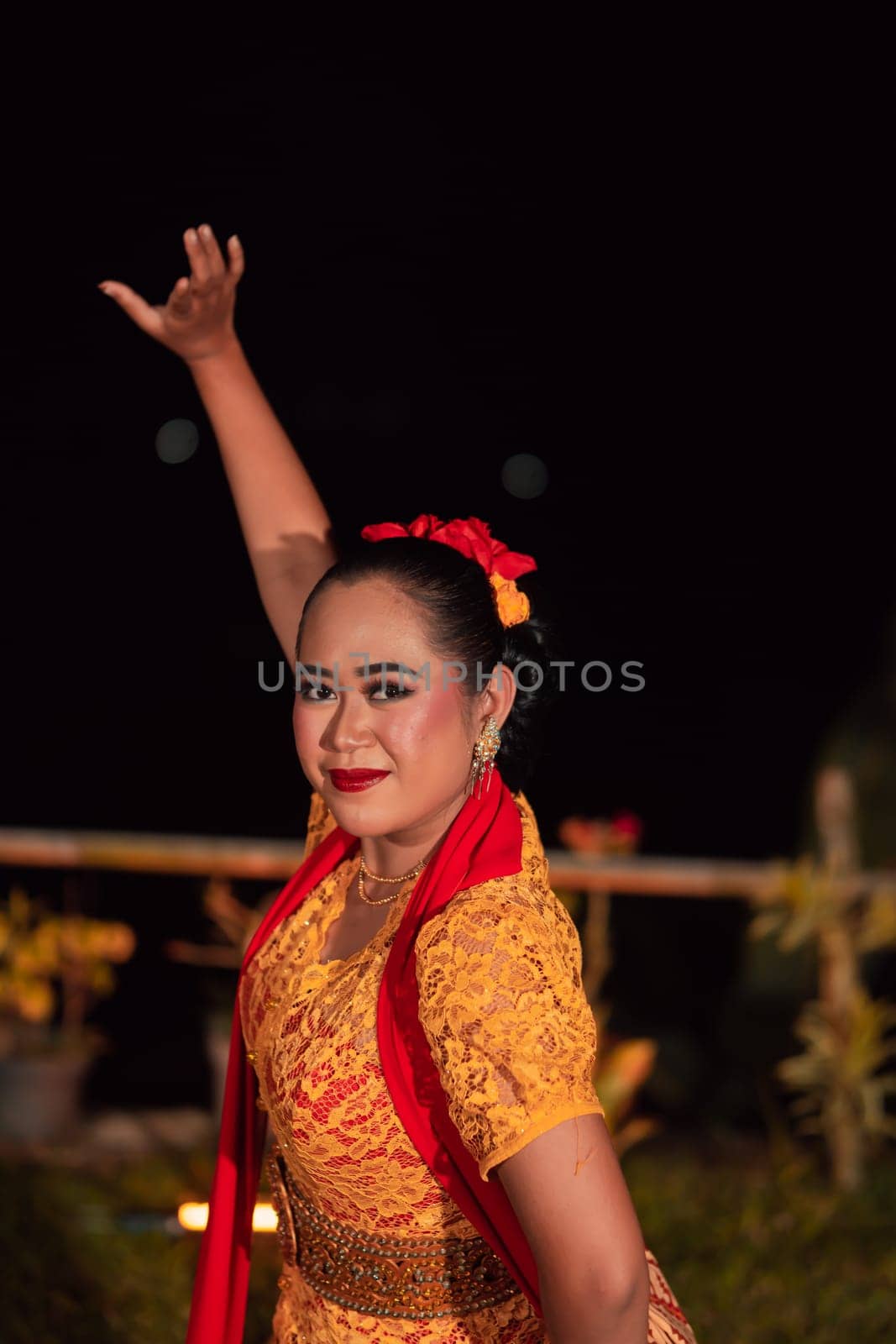 Close-up face of a Balinese woman during the traditional dance performance while wearing an orange costume and makeup on the stage