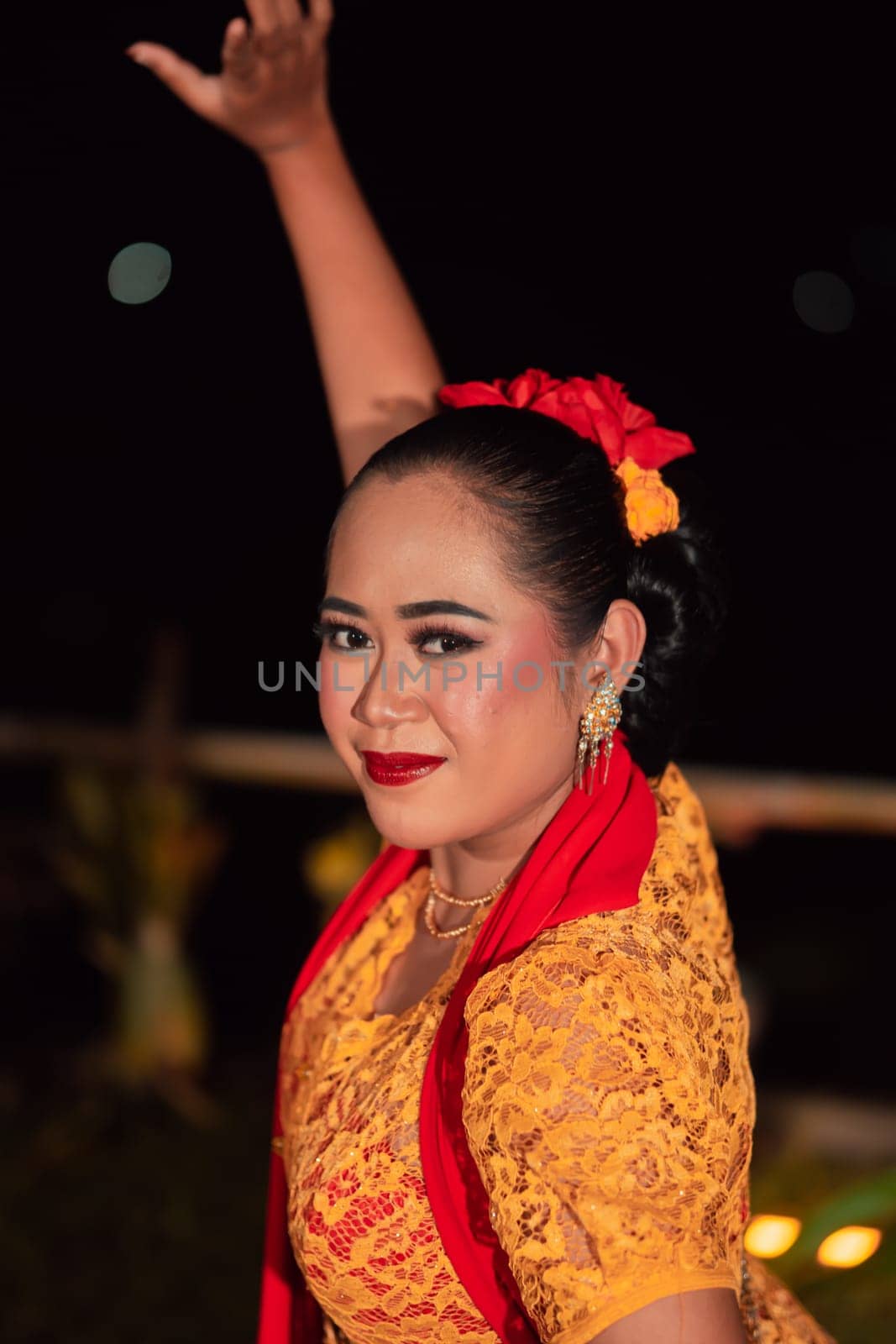 Close-up face of a Balinese woman during the traditional dance performance while wearing an orange costume and makeup on the stage