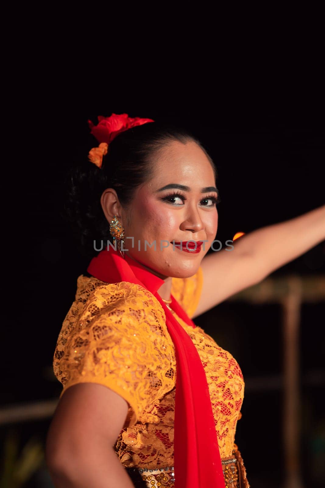 Close-up face of a Balinese woman during the traditional dance performance while wearing an orange costume and makeup on the stage