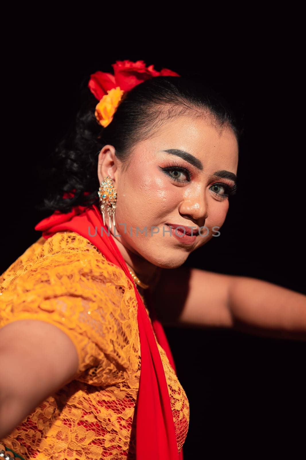 Beautiful face of an Indonesian woman in makeup while dancing a traditional dance in an orange costume during the festival in the night