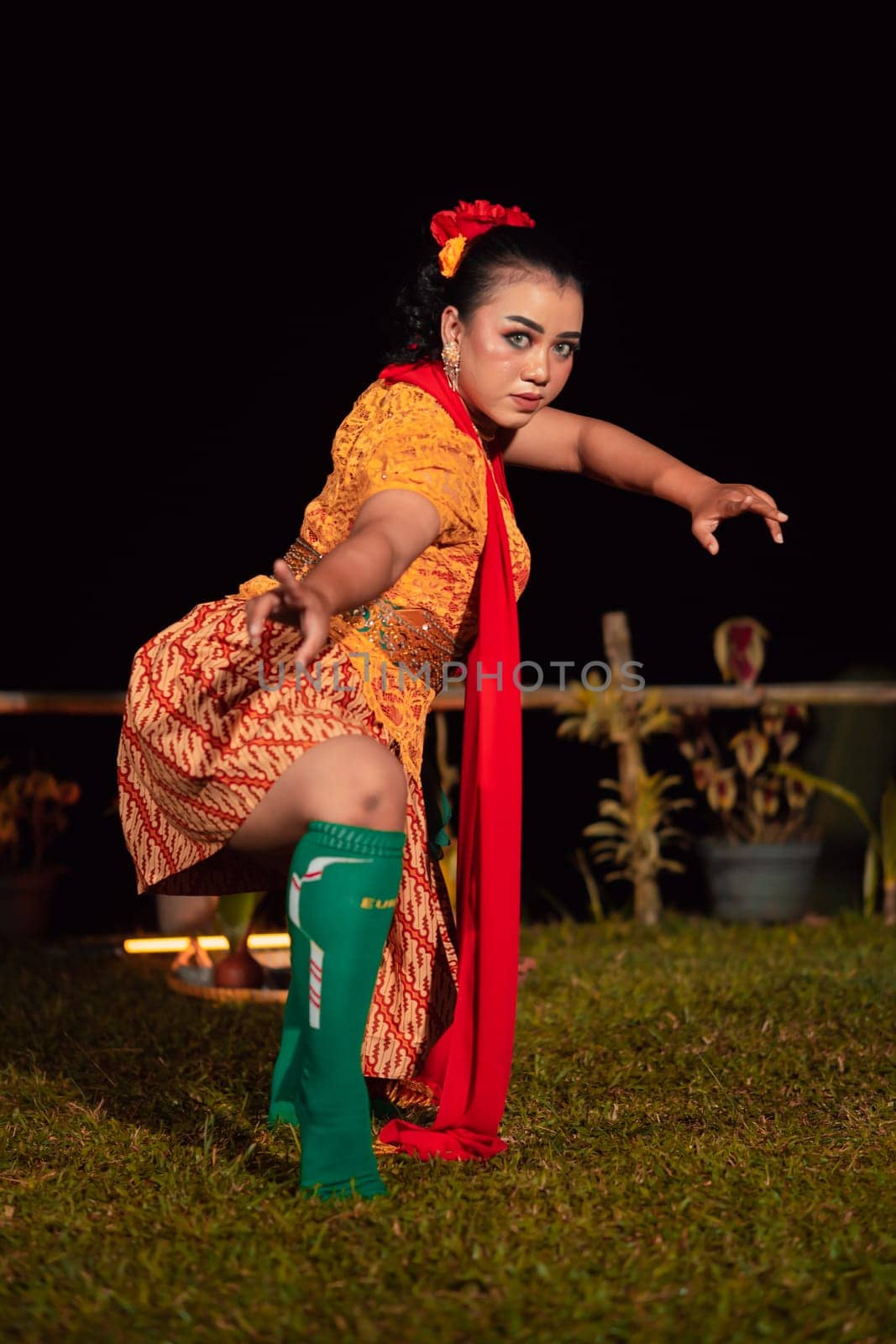 Balinese woman in traditional orange dress dancing with a red scarf while performing dancing in the night
