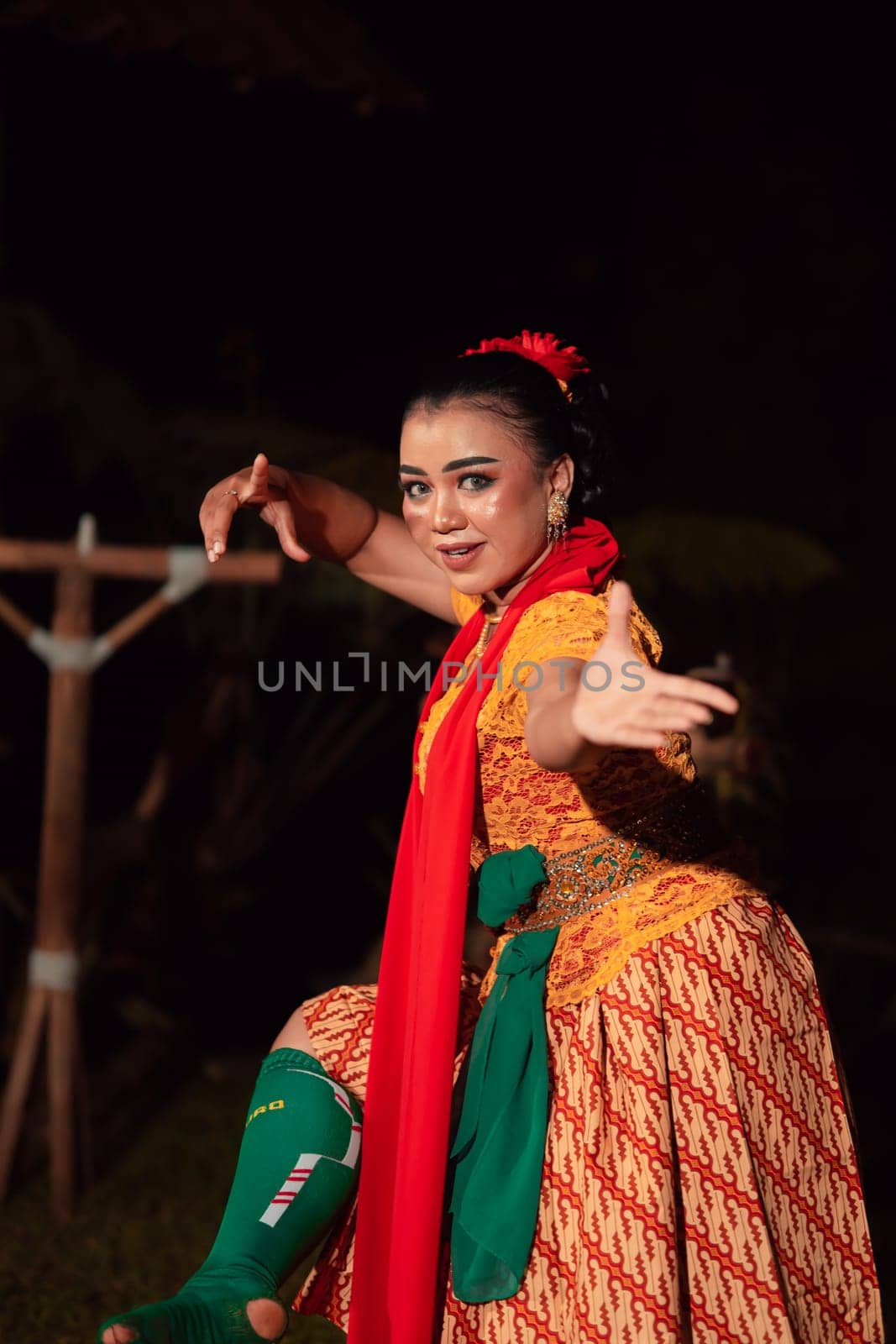 Balinese woman in traditional orange dress dancing with a red scarf while performing dancing in the night