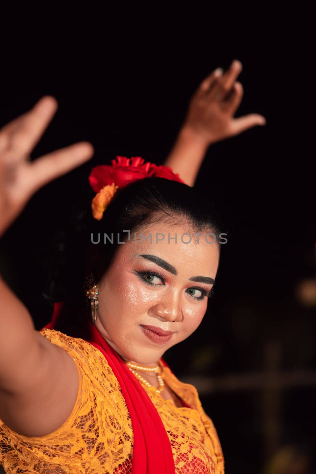 An Asian Traditional dancer in an orange dress with a red scarf and makeup performing at the dance festival in the night