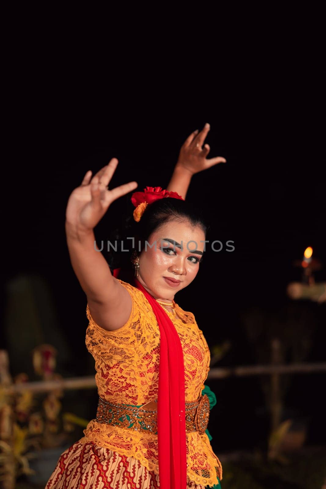 An Asian Traditional dancer in an orange dress with a red scarf and makeup performing at the dance festival in the night