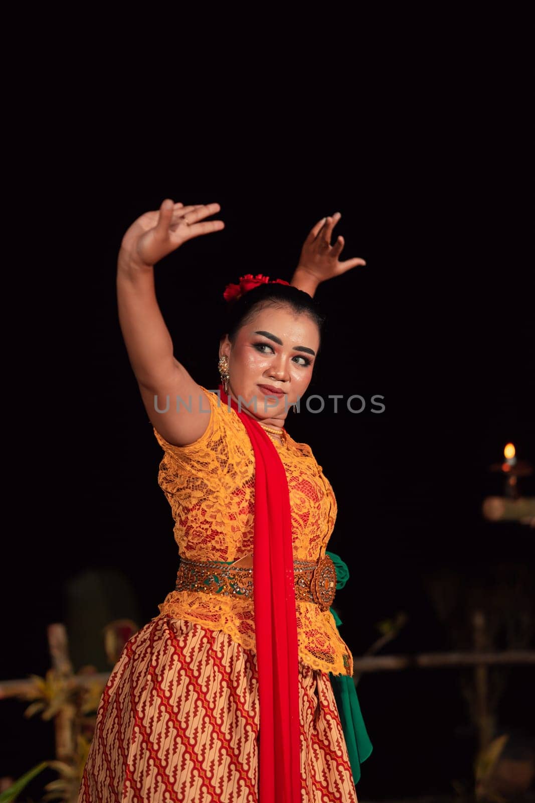 Balinese woman in traditional orange dress dancing with a red scarf while performing dancing in the night