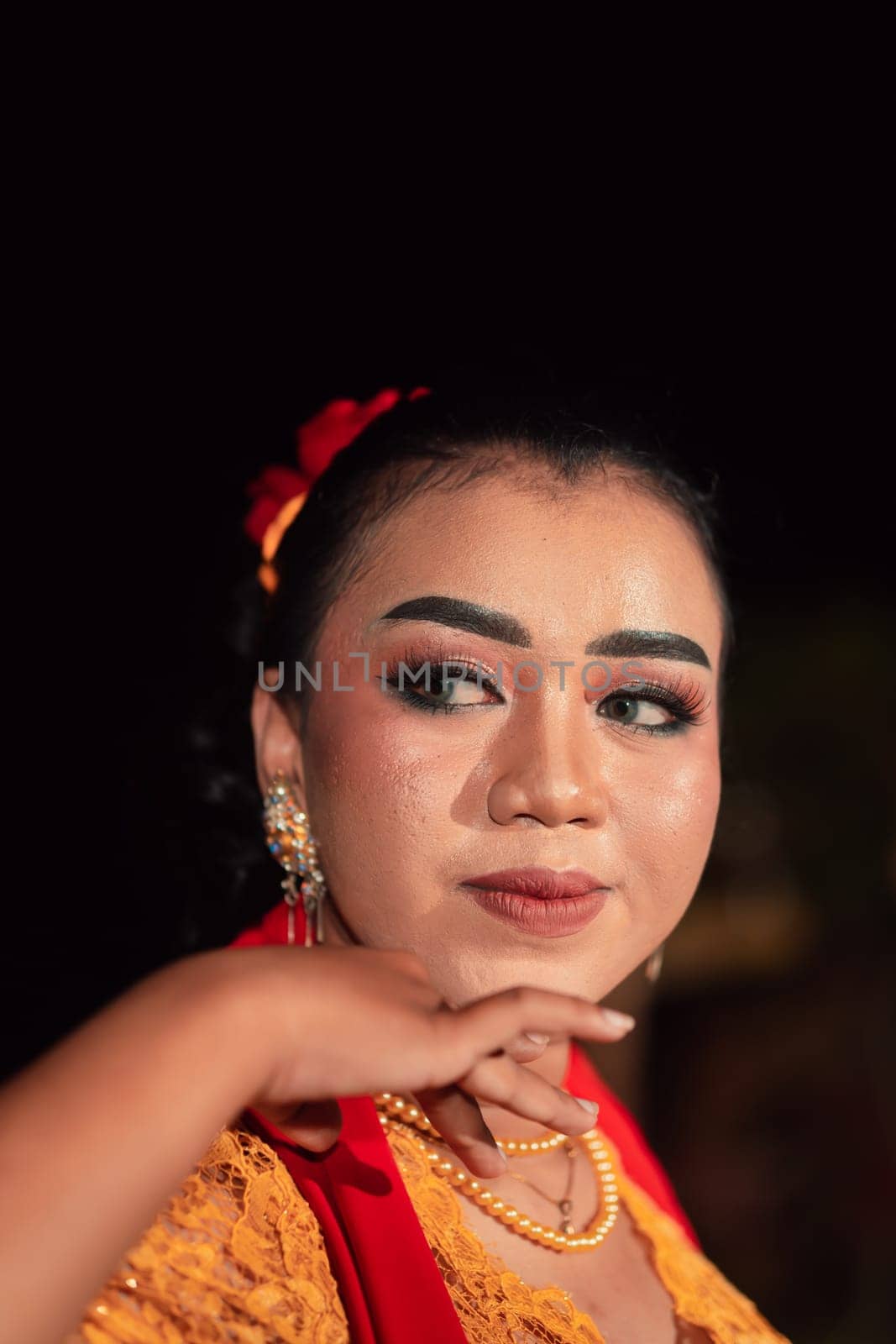 Gorgeous Asian woman wearing makeup and flowers in her hair while wearing a traditional orange dress and red scarf on her body at the night