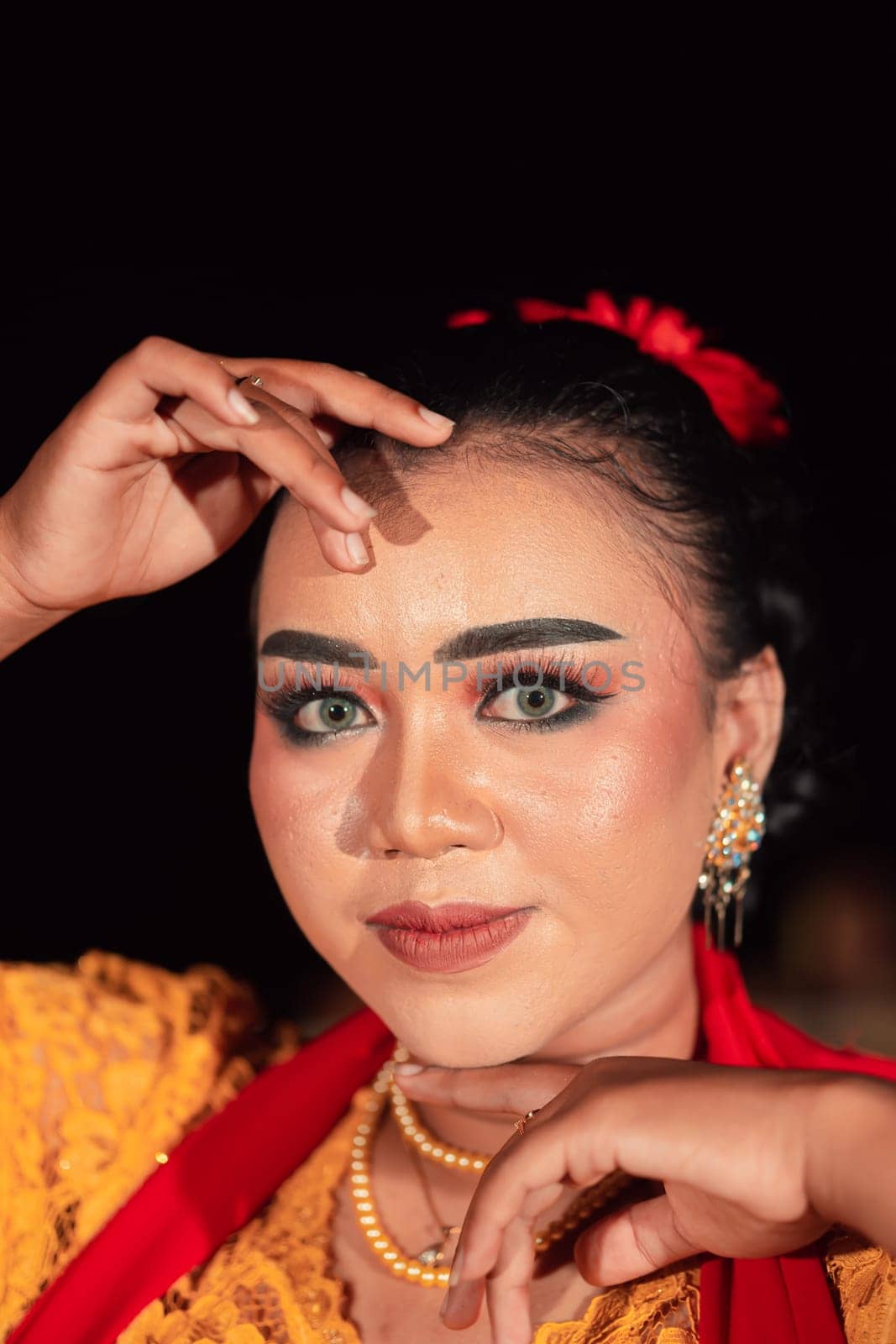 Gorgeous Asian woman wearing makeup and flowers in her hair while wearing a traditional orange dress and red scarf on her body at the night