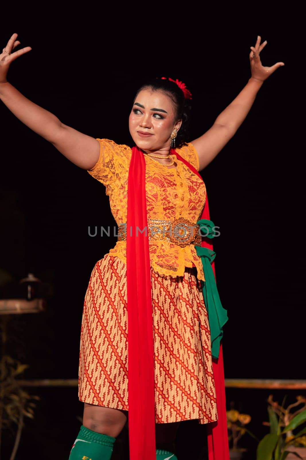 An Asian Traditional dancer in an orange dress with a red scarf and makeup performing at the dance festival in the night