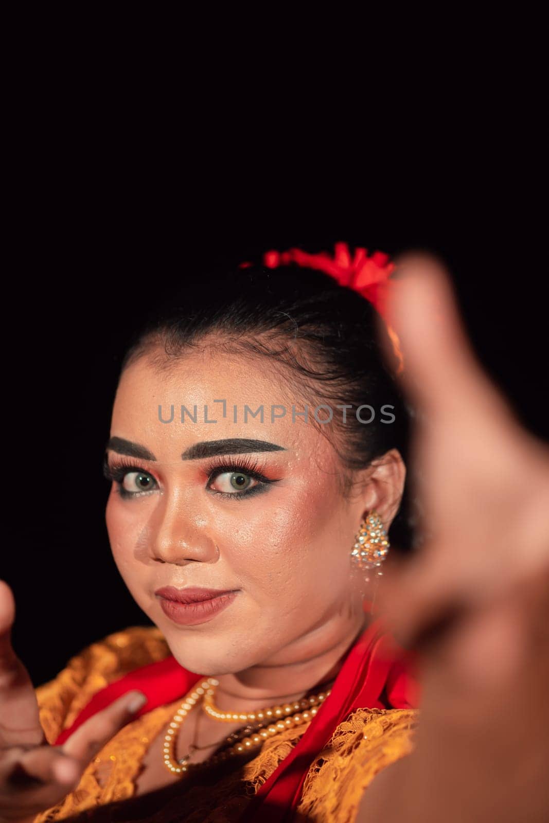 A Balinese woman poses with both her hands in a traditional orange dress and red scarf on her body in the festival