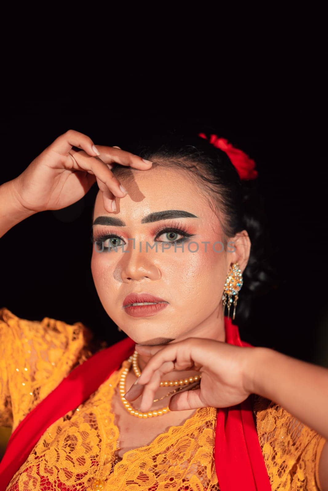 Gorgeous Asian woman wearing makeup and flowers in her hair while wearing a traditional orange dress and red scarf on her body at the night