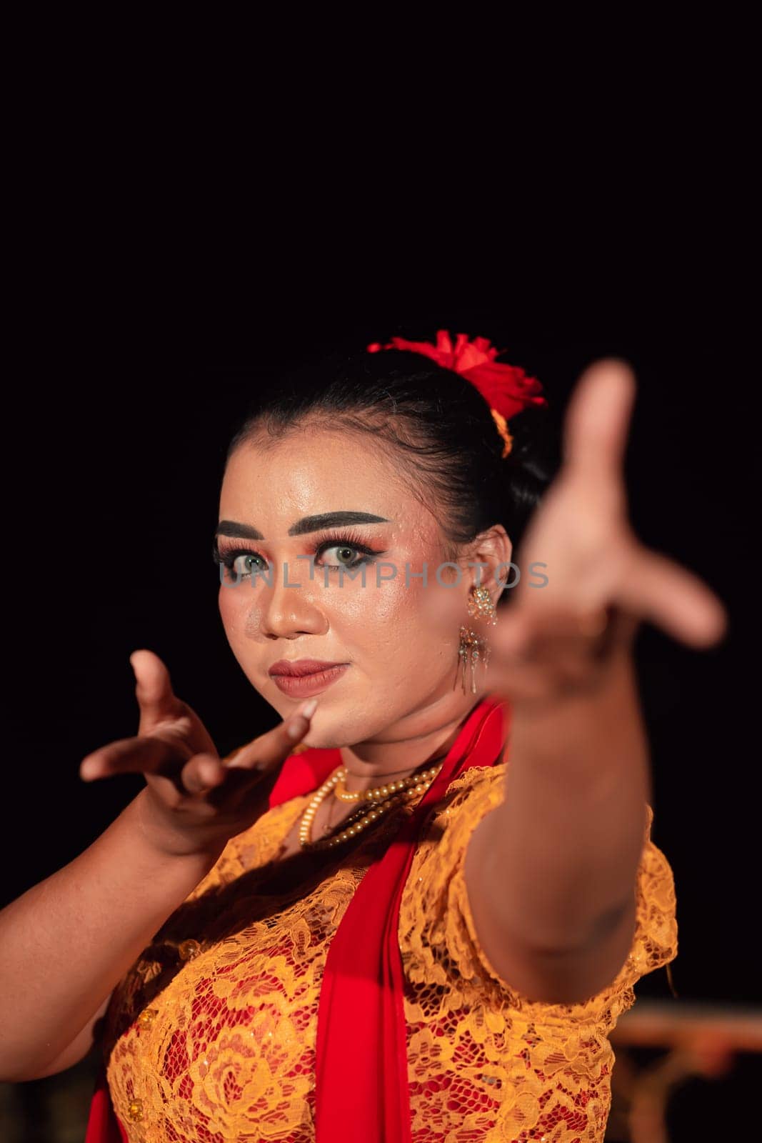 A Balinese woman poses with both her hands in a traditional orange dress and red scarf on her body in the festival