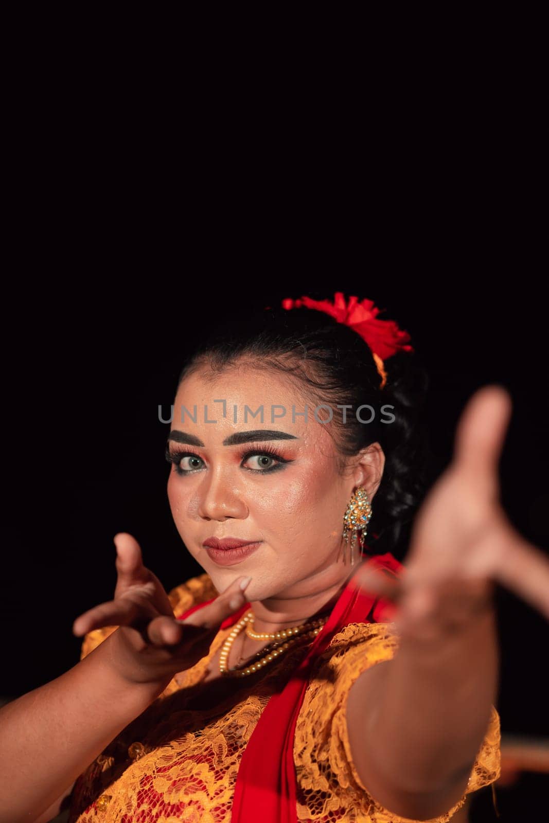 A Balinese woman poses with both her hands in a traditional orange dress and red scarf on her body in the festival