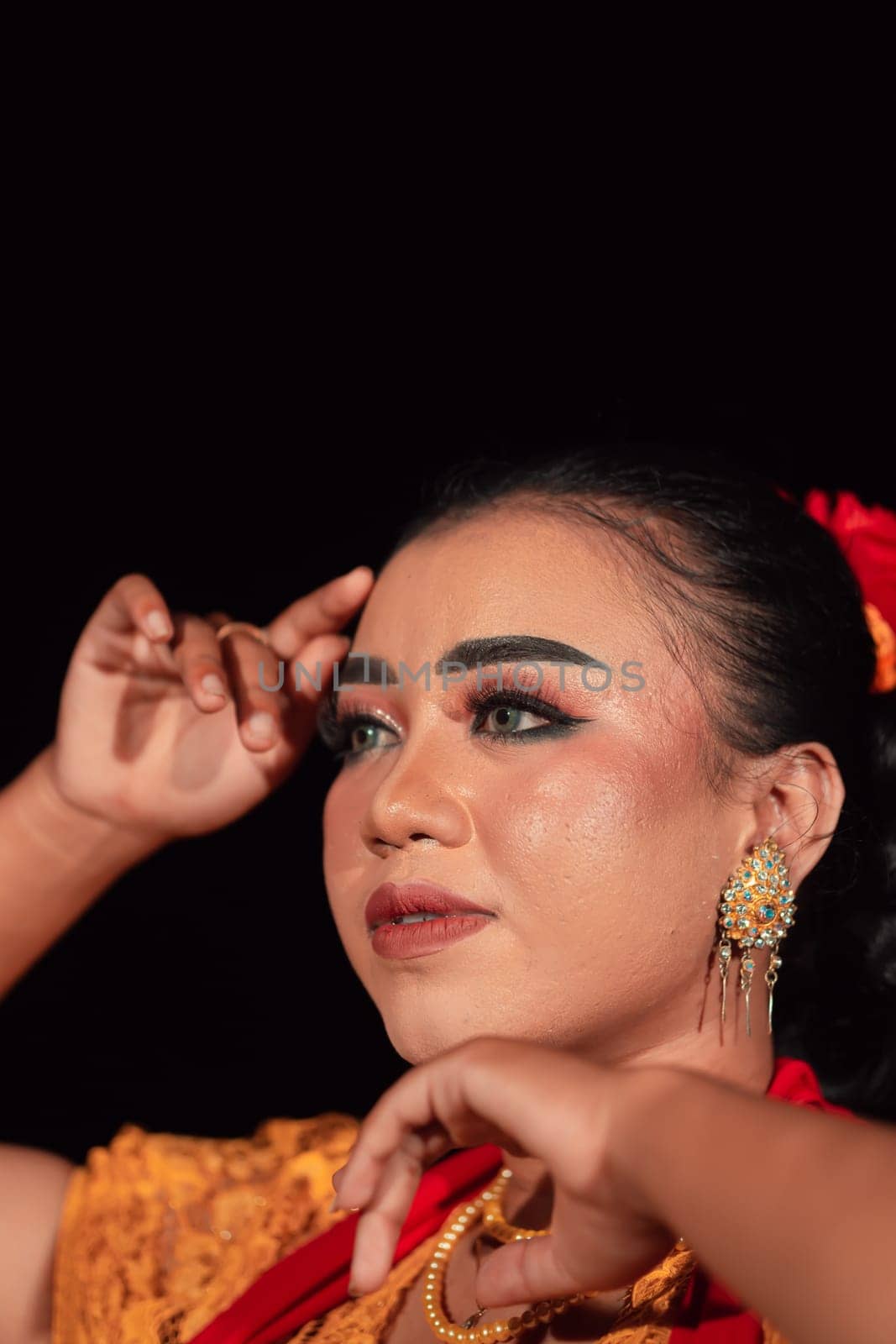 a Sharp gaze from an Indonesian woman with makeup on her face while wearing an orange dress and golden earrings in the night