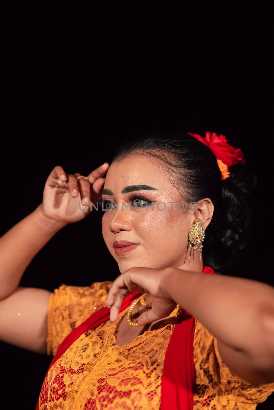 a Sharp gaze from an Indonesian woman with makeup on her face while wearing an orange dress and golden earrings in the night