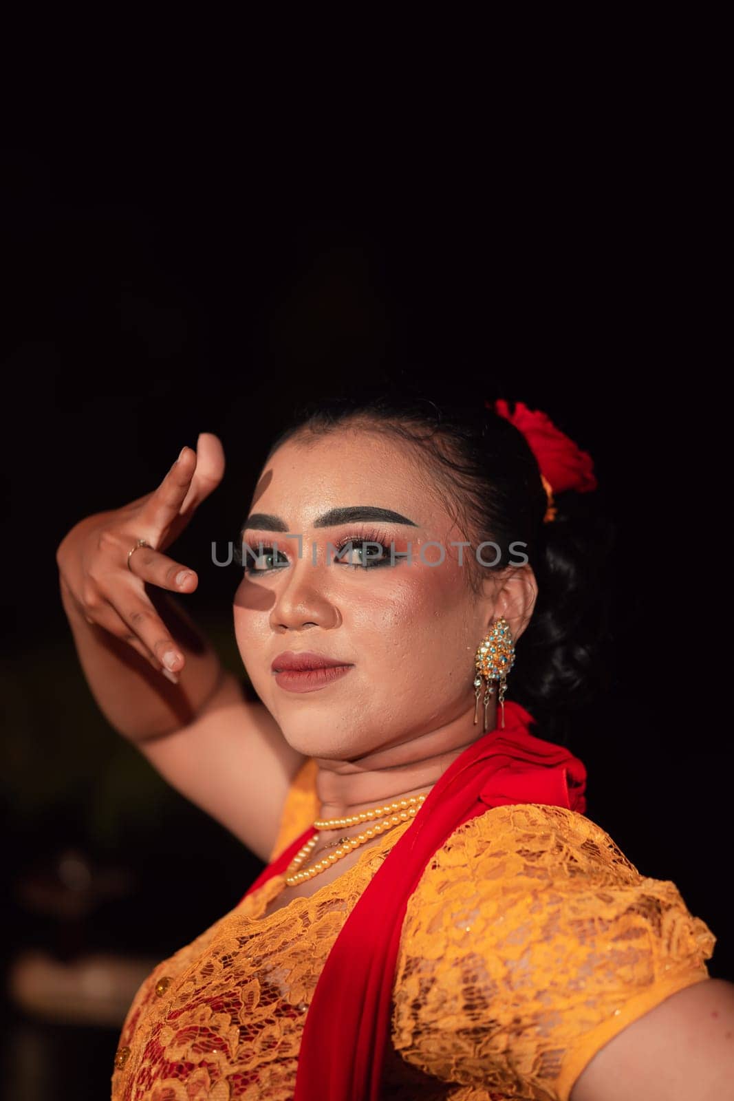 a Sharp gaze from an Indonesian woman with makeup on her face while wearing an orange dress and golden earrings in the night