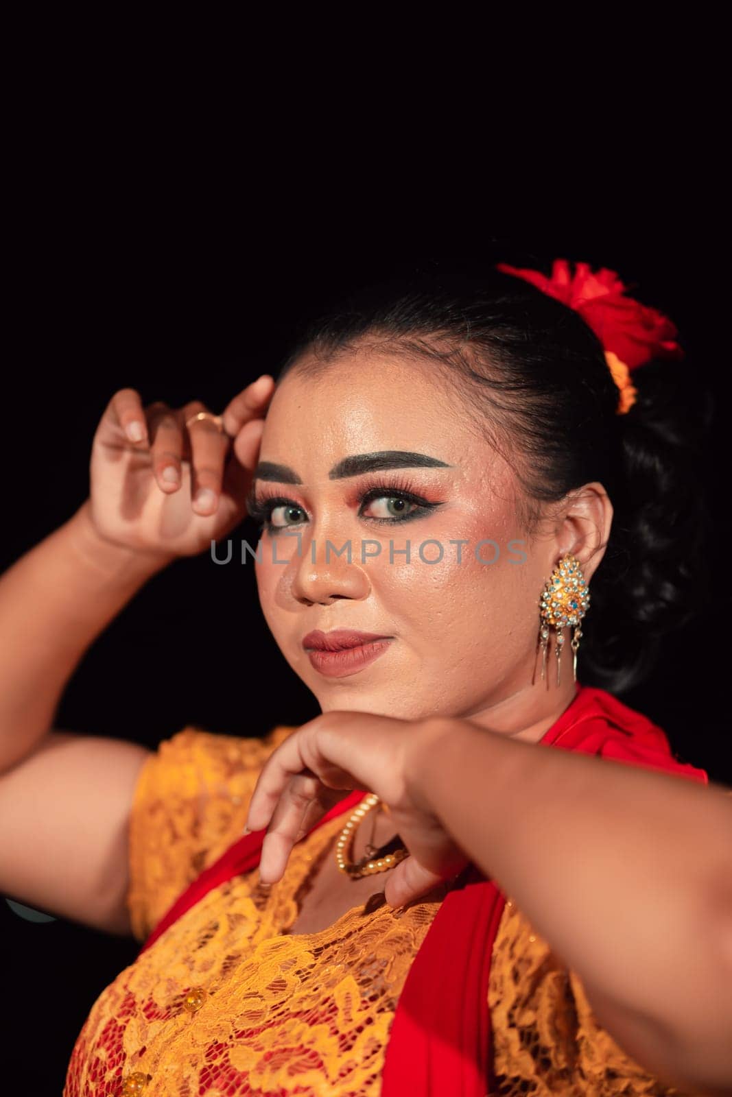 a Sharp gaze from an Indonesian woman with makeup on her face while wearing an orange dress and golden earrings in the night