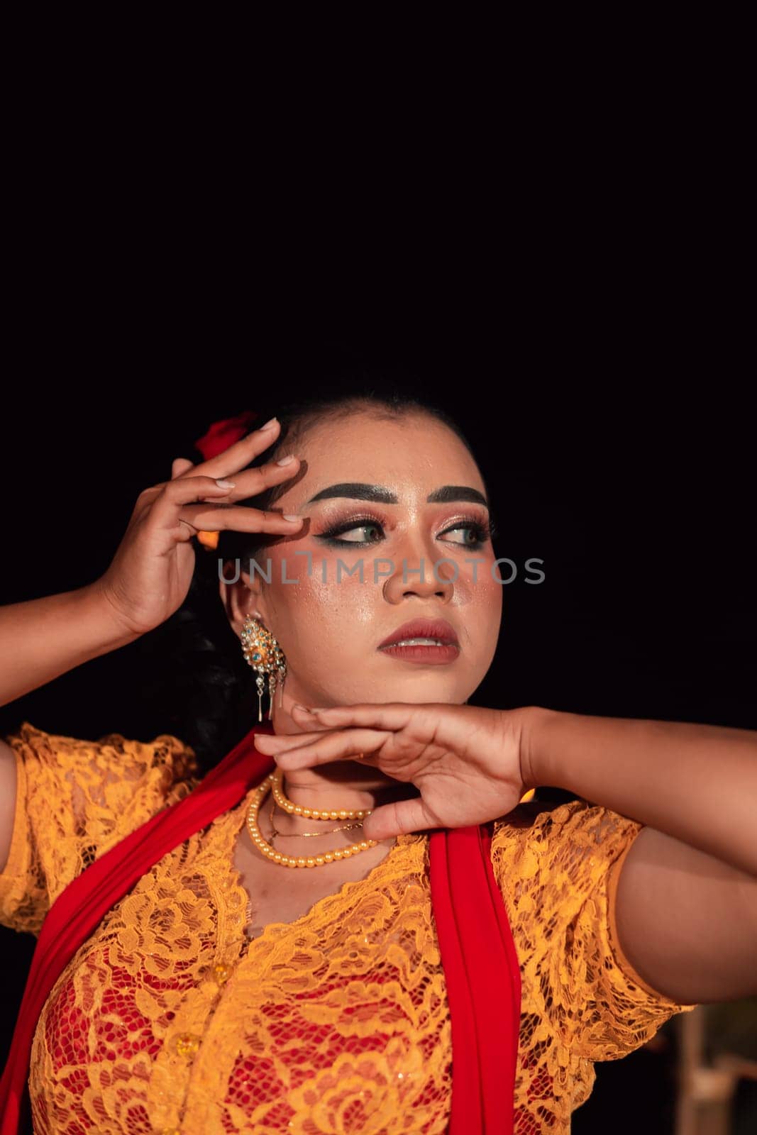 Close-up face of an Indonesian woman with makeup and an orange dress while wearing a piece of gold jewelry on her neck in the night