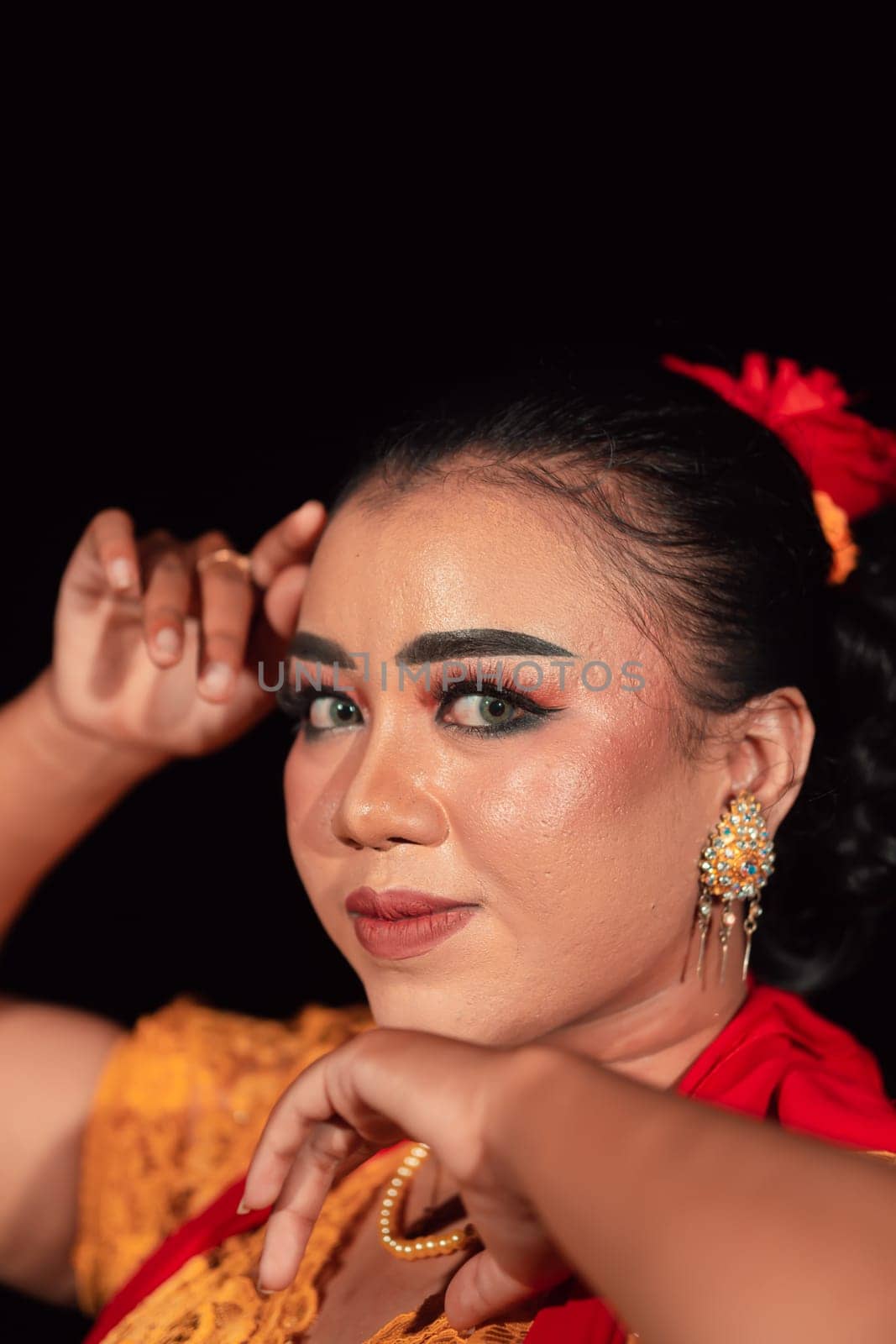 a Sharp gaze from an Indonesian woman with makeup on her face while wearing an orange dress and golden earrings in the night