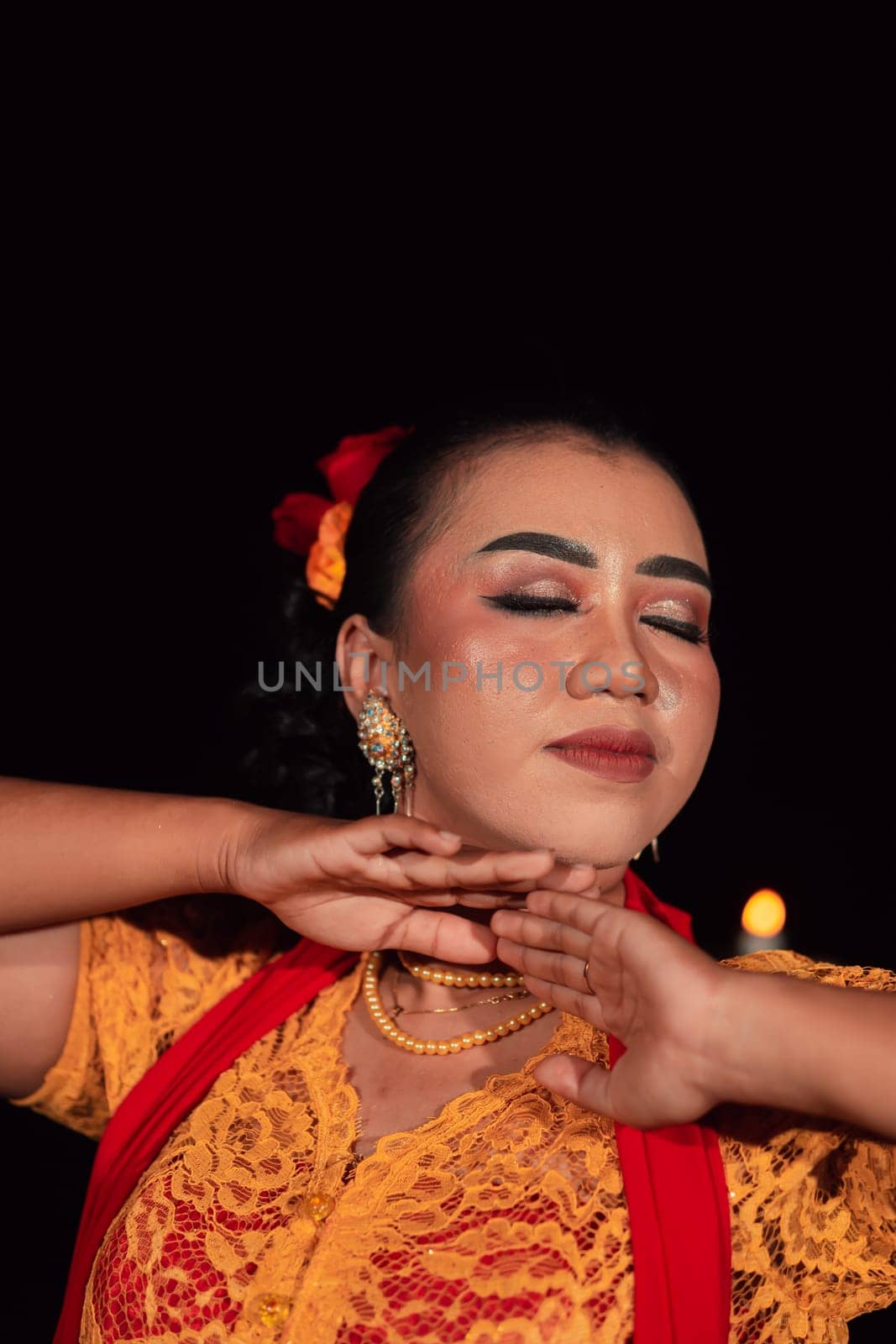 Close-up face of an Indonesian woman with makeup and an orange dress while wearing a piece of gold jewelry on her neck in the night