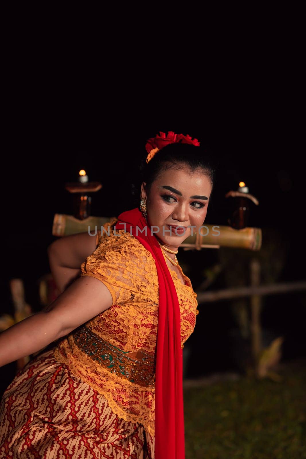 An Asian Traditional dancer in an orange dress with a red scarf and makeup performing at the dance festival in the night