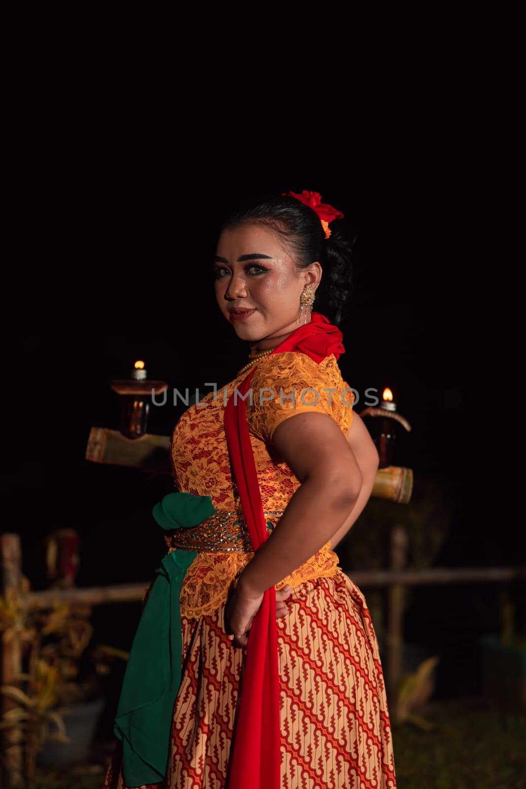 An Asian Traditional dancer in an orange dress with a red scarf and makeup performing at the dance festival in the night