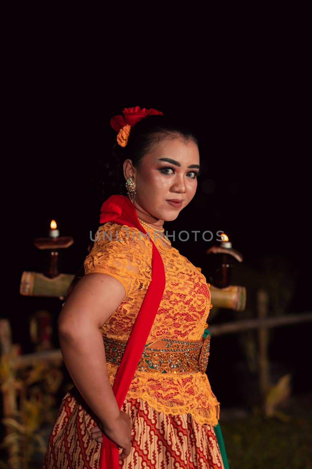 An Asian Traditional dancer in an orange dress with a red scarf and makeup performing at the dance festival in the night