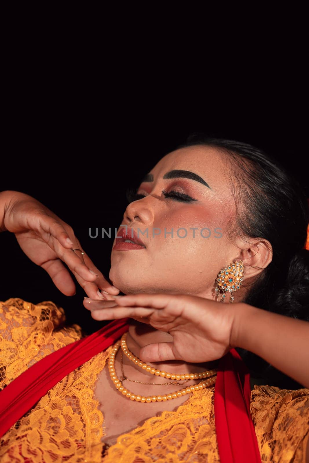 Close-up face of an Indonesian woman with makeup and an orange dress while wearing a piece of gold jewelry on her neck in the night