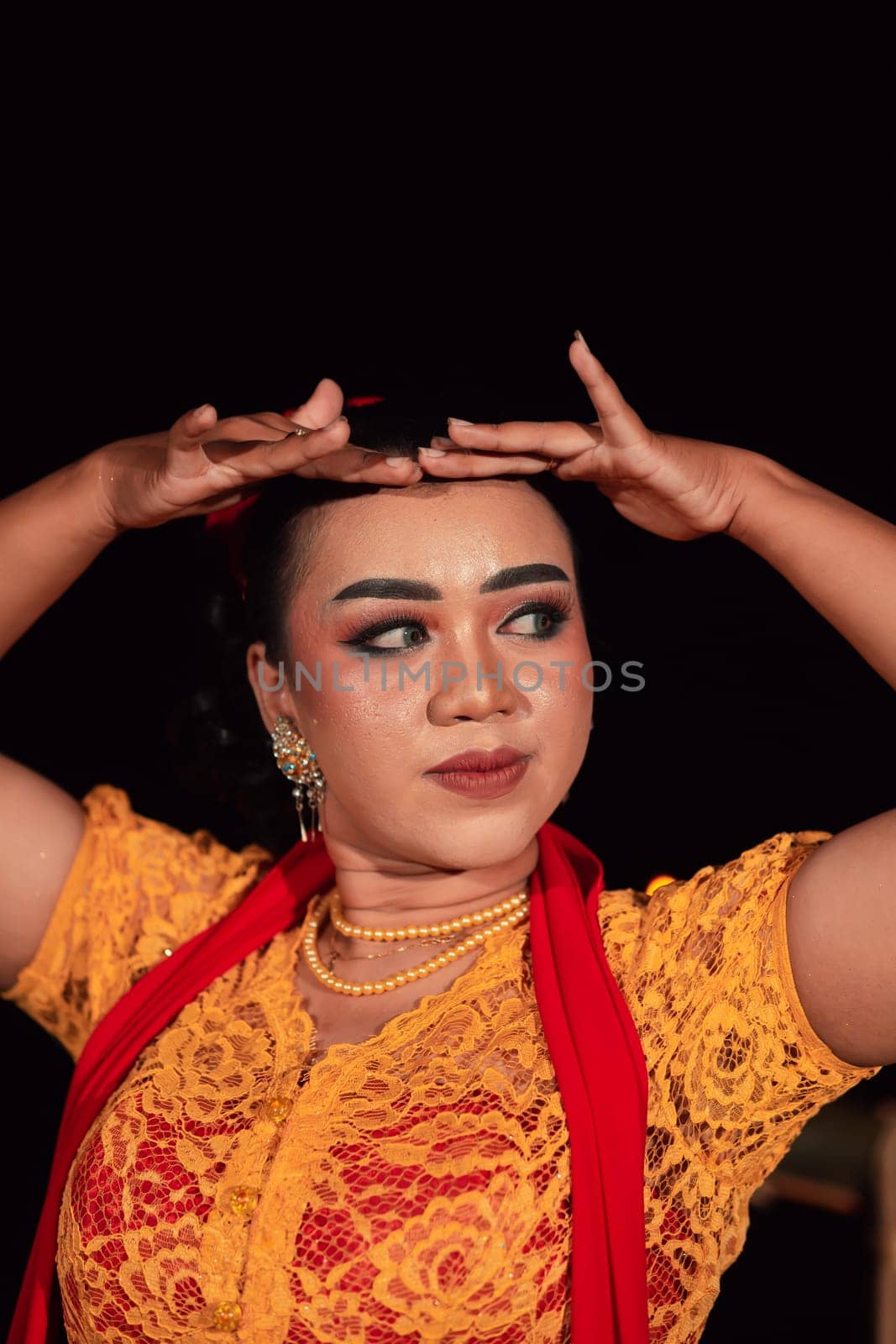 Close-up face of an Indonesian woman with makeup and an orange dress while wearing a piece of gold jewelry on her neck in the night
